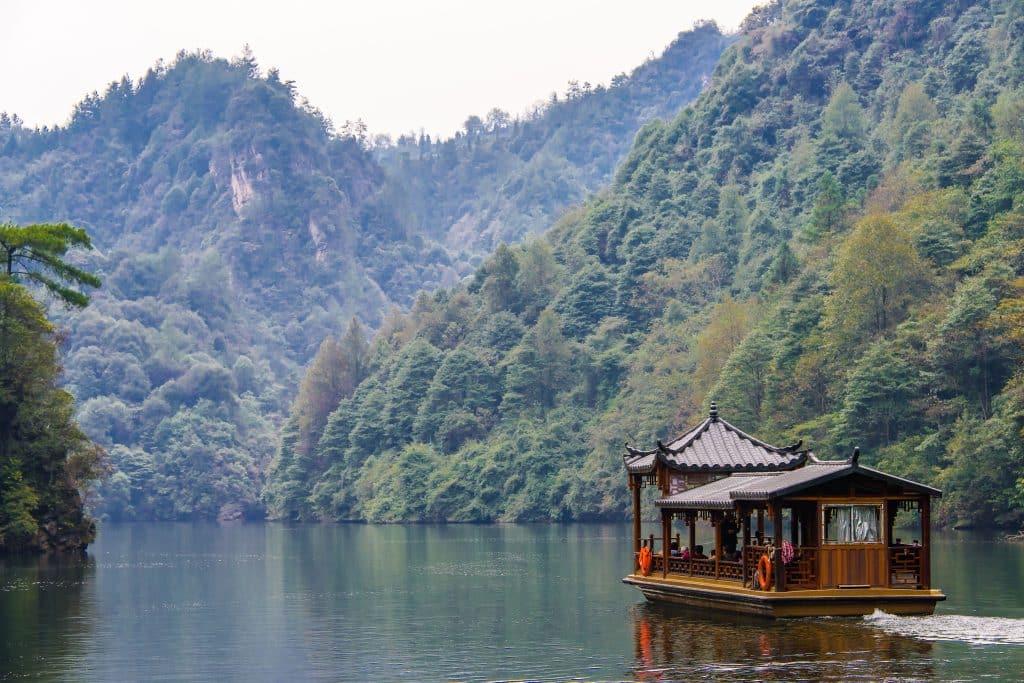 A covered wooden tour boat crossing Baofeng Lake between forested peaks, Zhangjiajie