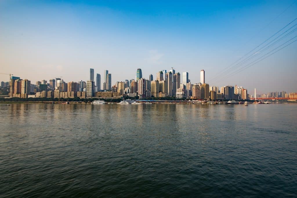Chongqing riverfront skyline in daylight, river cruise boats docked along the bank