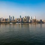 Chongqing riverfront skyline in daylight, river cruise boats docked along the bank