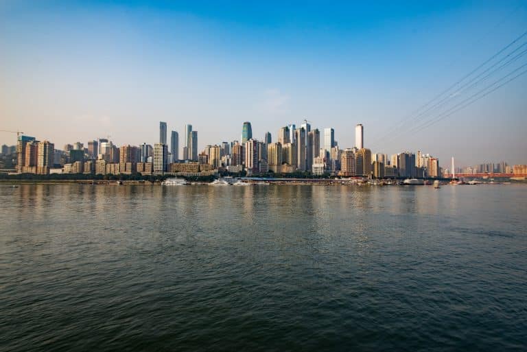 Chongqing riverfront skyline in daylight, river cruise boats docked along the bank