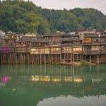 Lit stilt houses standing on wooden piles above the Tuo river at dusk, Fenghuang, Hunan