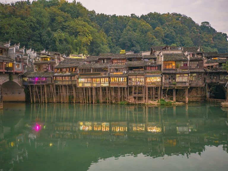 Lit stilt houses standing on wooden piles above the Tuo river at dusk, Fenghuang, Hunan