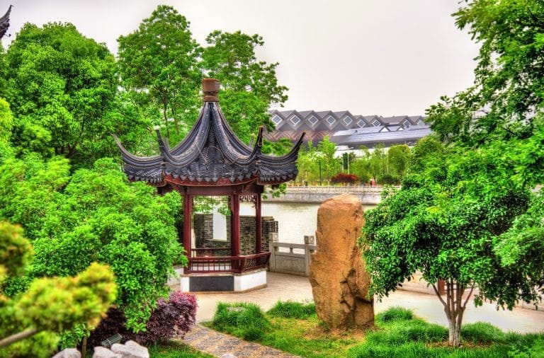 A traditional garden pavilion beside a canal in Suzhou, surrounded by greenery