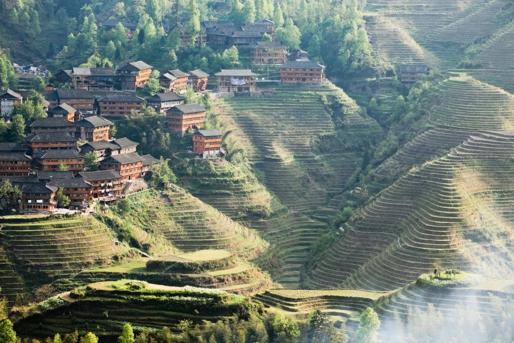 Terraced rice fields on steep hillsides above a village of dark wooden houses, Longji, Guangxi