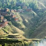 Terraced rice fields on steep hillsides above a village of dark wooden houses, Longji, Guangxi