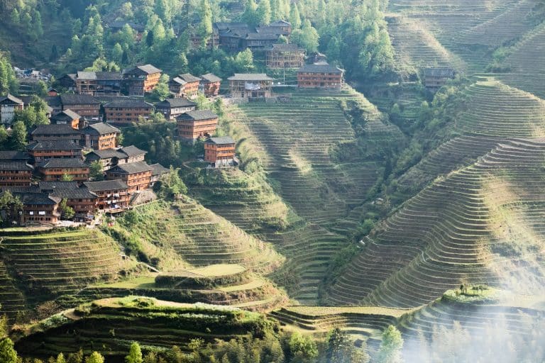 Terraced rice fields on steep hillsides above a village of dark wooden houses, Longji, Guangxi