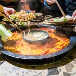 A divided Sichuan hotpot on the table, chopsticks lifting food out of the chilli broth
