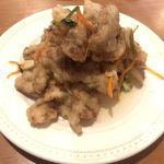 Plate of guo bao rou, crisp fried pork slices in a pale sweet-sour glaze with shredded carrot and scallion