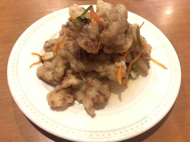 Plate of guo bao rou, crisp fried pork slices in a pale sweet-sour glaze with shredded carrot and scallion