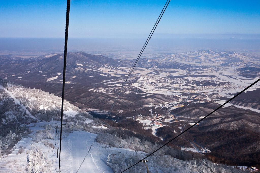 View from a chairlift at Yabuli ski resort over snow-covered, forested hills and the resort buildings in the valley below