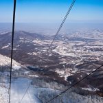 View from a chairlift at Yabuli ski resort over snow-covered, forested hills and the resort buildings in the valley below
