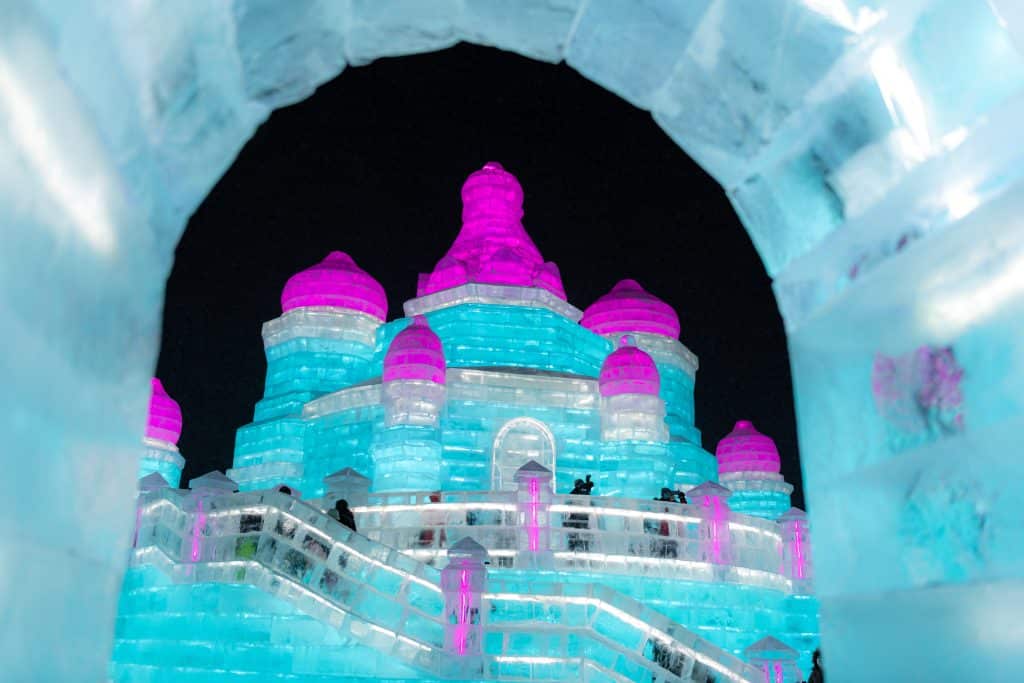 Lit ice castle behind an ice fence at night, Harbin Ice and Snow Festival, January 2022