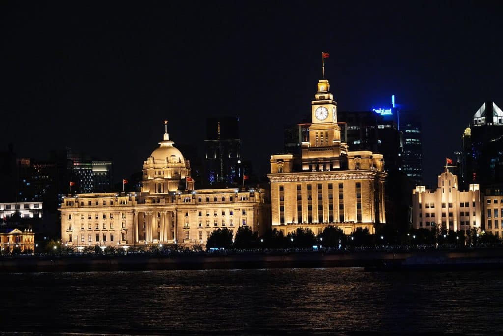 The former HSBC building with its dome and the Customs House clock tower lit at night on the Bund, seen across the Huangpu River